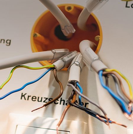 A junction box with multiple cables, including a cross switch, a changeover switch, and a lamp cable. A hand holds a cable with stripped conductors.