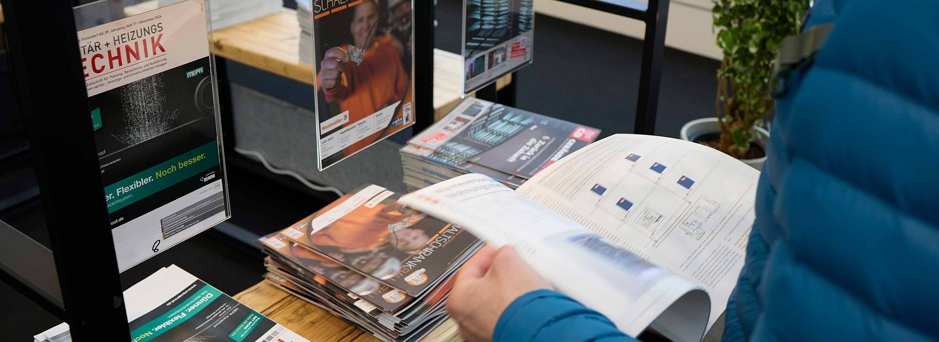 Angled view from above of a man leafing through a magazine in the media lounge. In front of him is a shelf with more magazines.