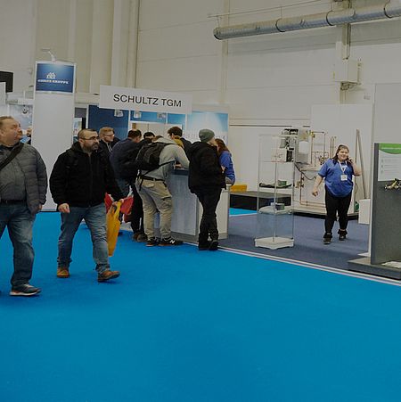 A blue carpet with exhibitors and exhibits. Some visitors walk by, while others stop to look and chat.