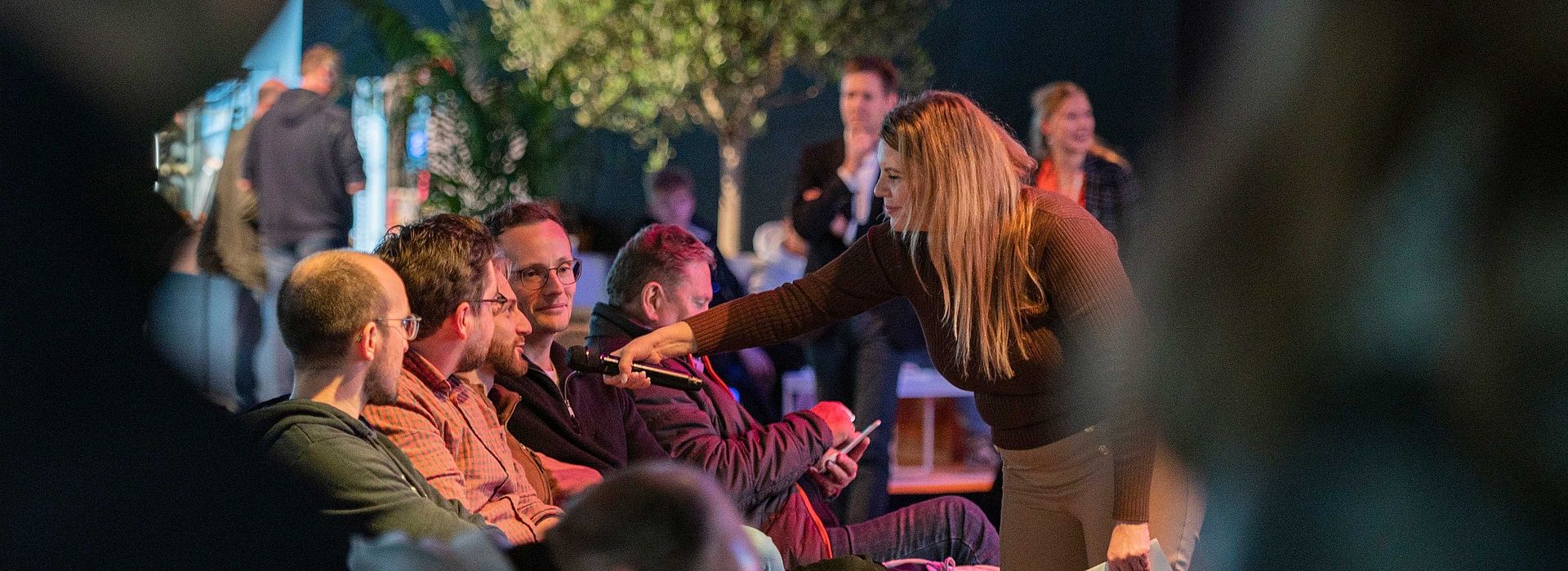 Deutsch Englisch  Situation in the GET NORD Arena: The presenter holds out the microphone to a participant in the audience so that they can actively participate in the programme.