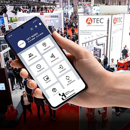 A hand holds a smartphone. The home screen of the GET NORD app can be seen on the screen with the areas “Exhibitors”, “Hall Plan”, “Program”, “Networking”, “Brands” and “Register”. In the background you can see a scene from the ongoing trade fair operations the GET NORTH.