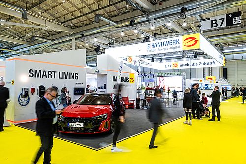 A photo of the GET Nord trade fair featuring several exhibitor stands in the background and blurred visitors in the foreground, including a red Audi.