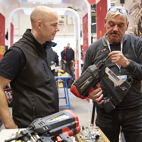 Ein Ausstellender berät einen Besuchenden zu einem Werkzeuggerät.