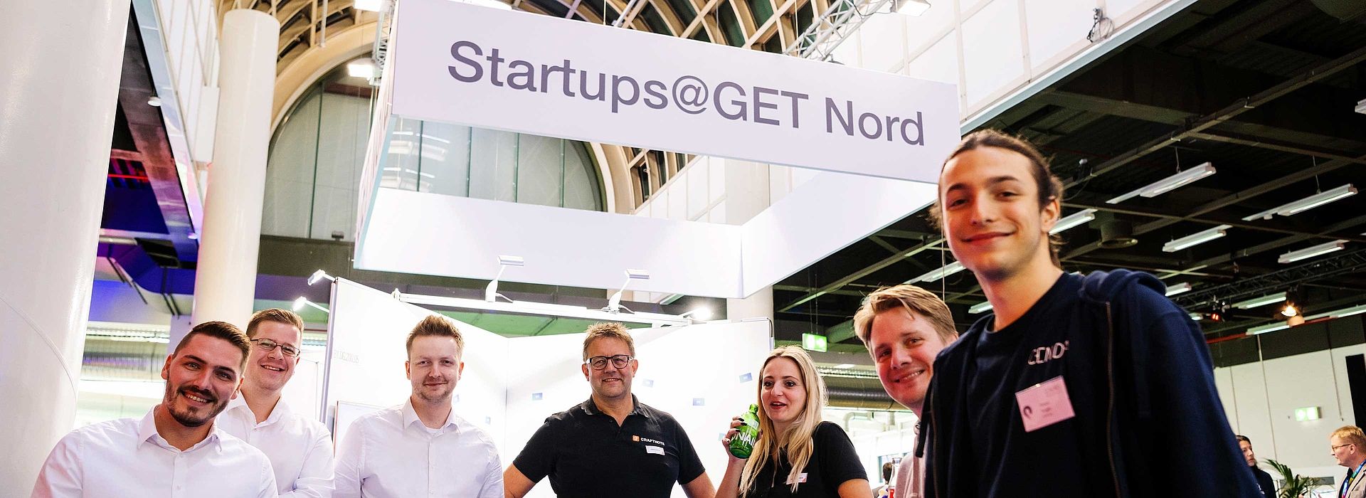 Seven people look into the camera. There is a sign in the background with Startups@GET NORD.