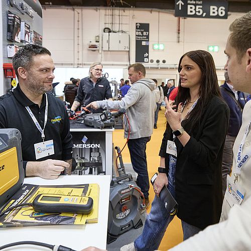 Zwei Männer und eine Frau unterhalten sich an einem Stand. 