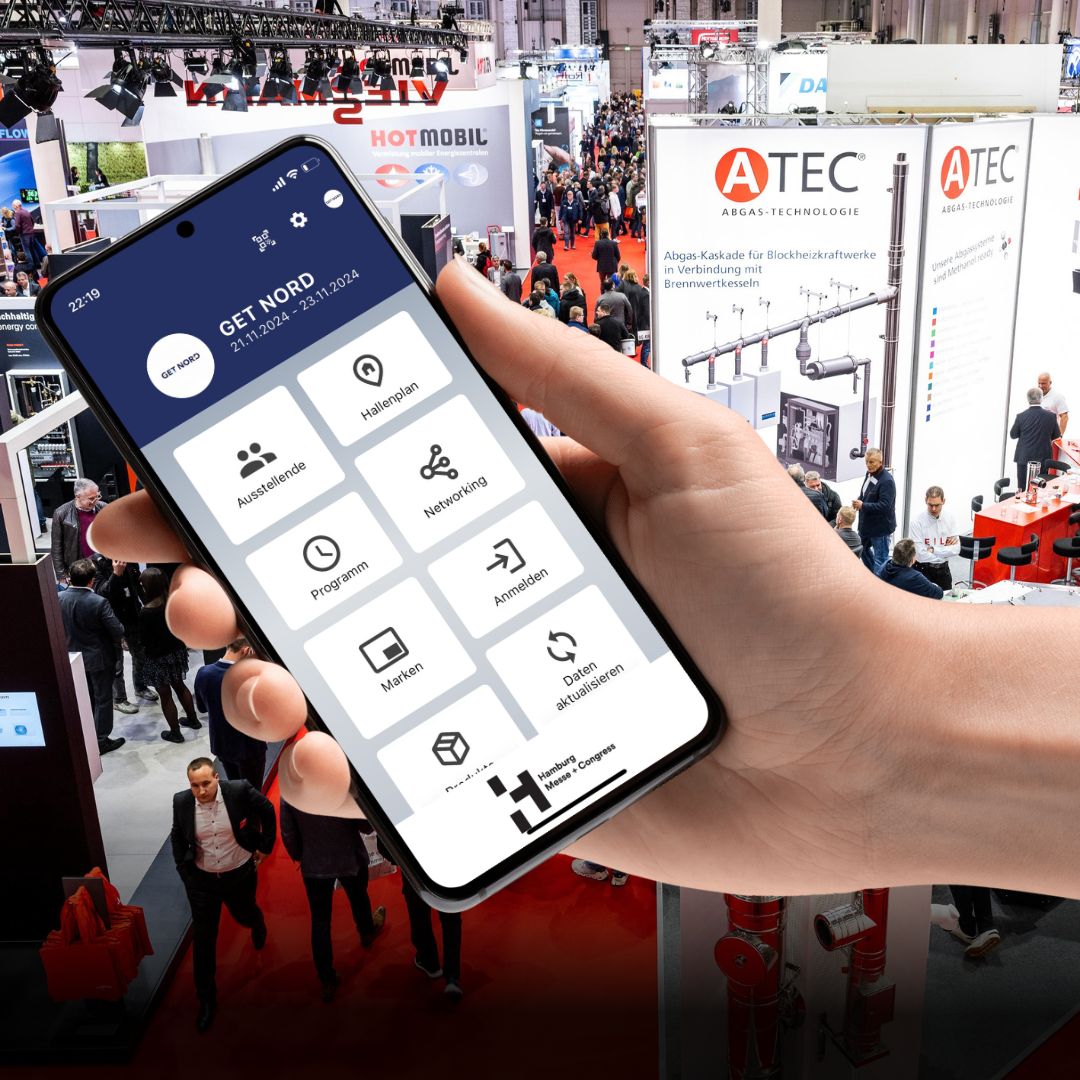 A hand holds a smartphone. The home screen of the GET NORD app can be seen on the screen with the areas “Exhibitors”, “Hall Plan”, “Program”, “Networking”, “Brands” and “Register”. In the background you can see a scene from the ongoing trade fair operations the GET NORTH.